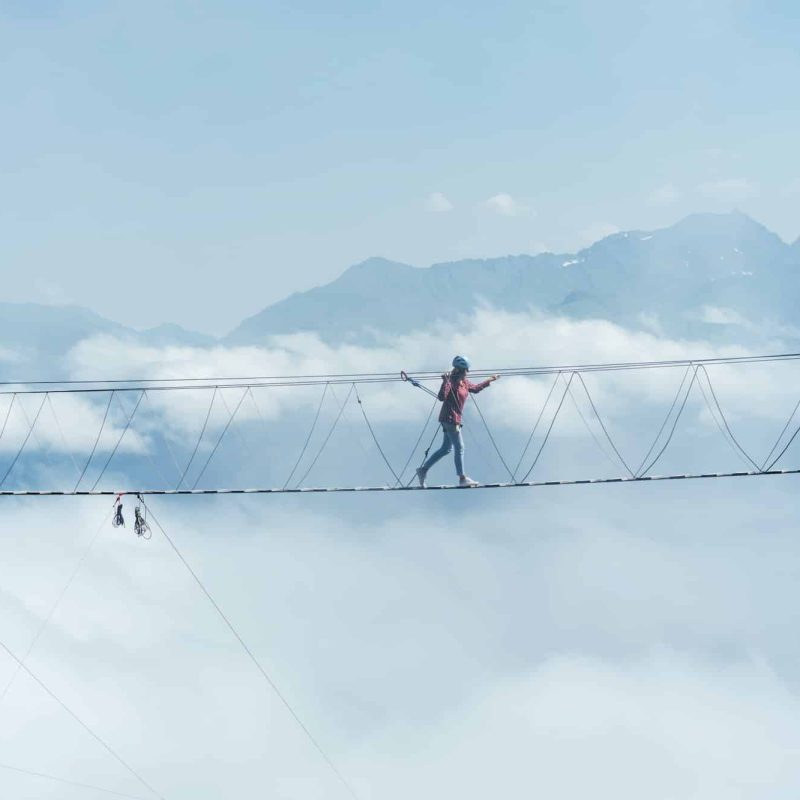 a tiny person walks on a suspension bridge