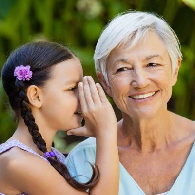 Granddaughter whispering in ears of smiling grandmother