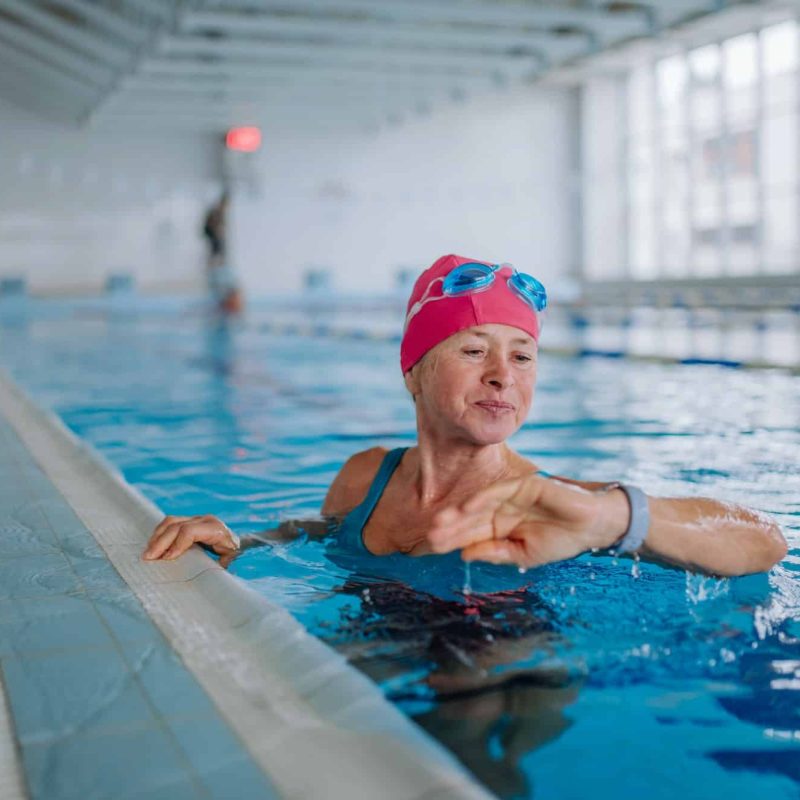 Senior woman looking at smartwatch when swimming in indoors swimming pool