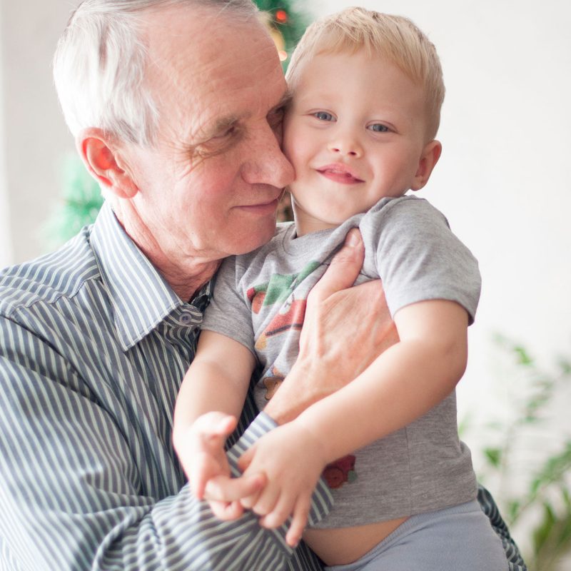 sentimental-old-man-holding-small-child-his-arms-front-decorated-christmas-tree